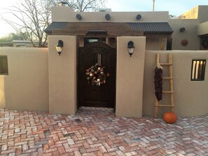 Une entrée d’immeuble avec une porte en bois, un chemin en briques et une guirlande décorative.