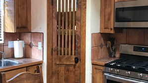 A kitchen with wooden cabinets, a stainless steel stove, and a door with vertical slats. - Charming Casita in historic Town of Mesilla,  NM  2392 Calle de Parian (Mesilla)
