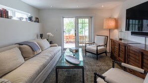 Ein Wohnzimmer mit einer Couch, Sesseln, einem Couchtisch, einem Fernseher und einem Bücherregal.