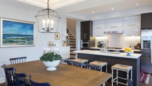Eine moderne Küche mit einer zentralen Kochinsel, Edelstahlgeräten und einem Essbereich mit Holztisch und blauen Stühlen.