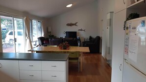 Una cocina con una mesa de comedor, sillas, un refrigerador y un televisor al fondo.