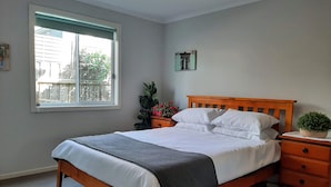Un dormitorio con una cama de madera, una mesita de noche, una ventana y una planta en maceta.