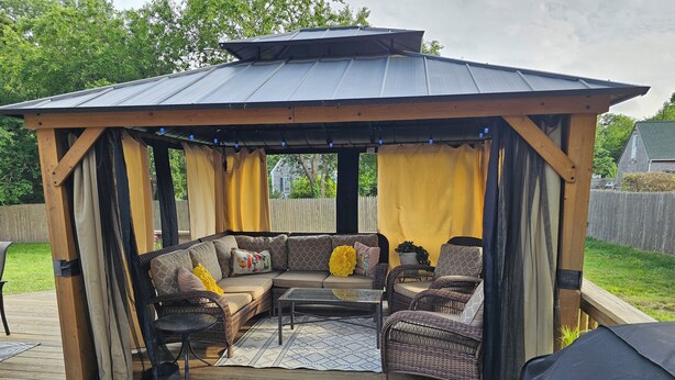 A covered outdoor seating area with a wooden deck, cushioned seating, and a pergola structure. - Oak Bluffs - Quiet neighborhood (Oak Bluffs)