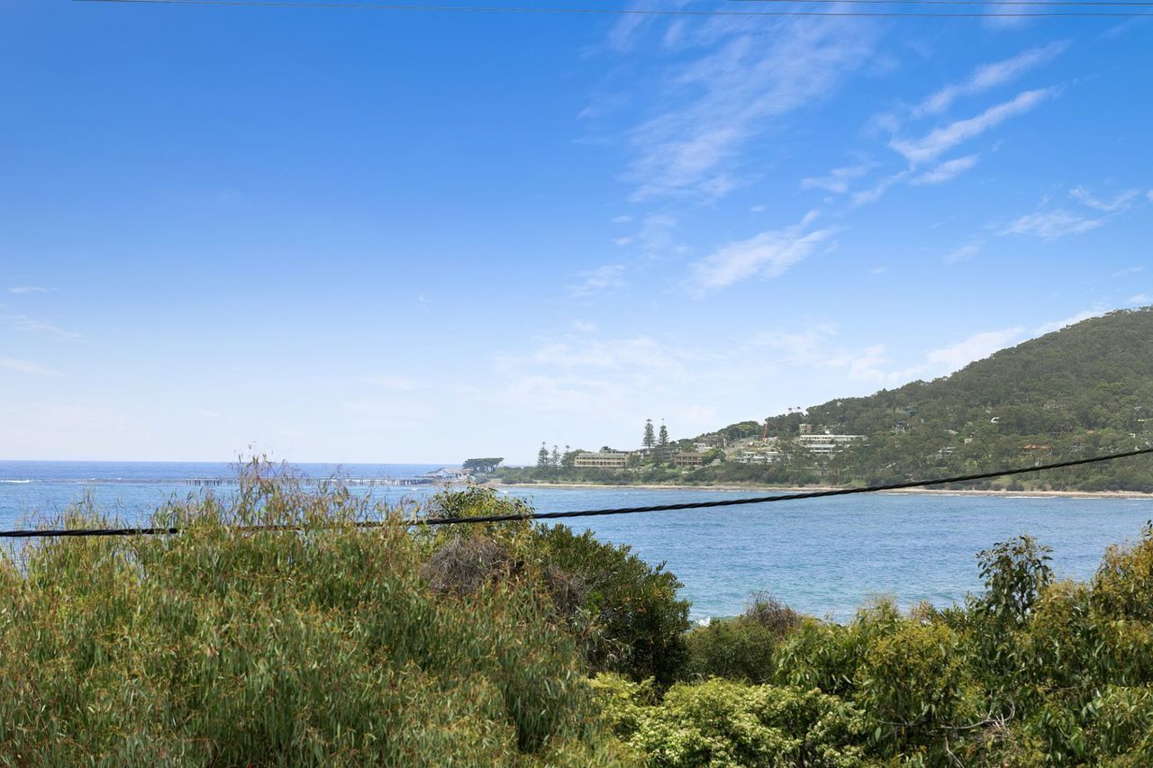 Eine Küstenlandschaft mit blauem Himmel, Wasser und hügeliger Landschaft mit Gebäuden.