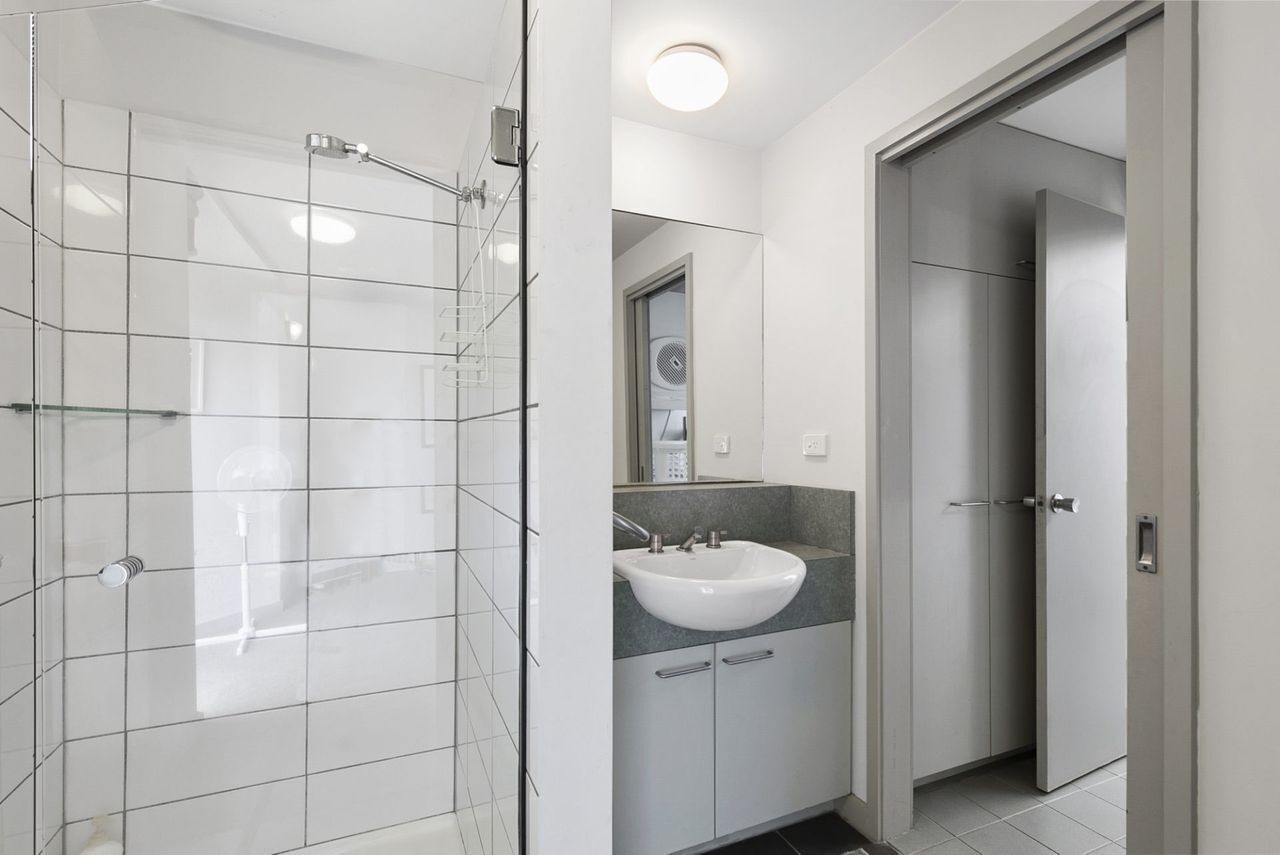 A modern bathroom with a glass shower enclosure, a white sink, and a walk-in closet.