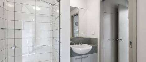 A modern bathroom with a glass shower enclosure, a white sink, and a walk-in closet.