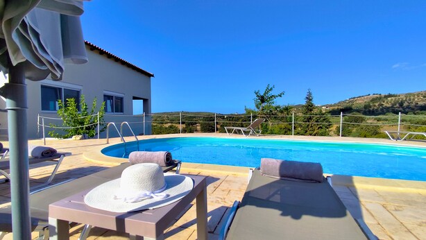 A pool area with lounge chairs, a sunbed, and a white hat on a table. - Spacious Family Villa, Private pool,  beach 5 km (Filaki)