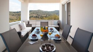 A balcony with a table set for breakfast, overlooking a hilly landscape. - Spacious Family Villa, Private pool,  beach 5 km (Filaki)