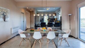 A modern dining area with a glass table, white chairs, and a central light fixture. - Spacious Family Villa, Private pool,  beach 5 km (Filaki)