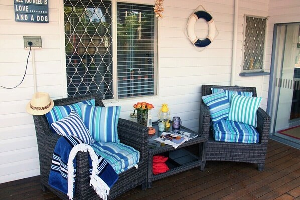 A cozy outdoor seating area with wicker furniture, striped cushions, and a small table with decorative items.