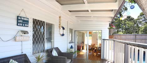A covered porch with wicker furniture, a sign reading 'ALL YOU NEED IS LOVE...AND A DOG', and a 'BEACH HOUSE' sign.