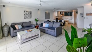 A modern living room with two grey sofas, a white coffee table, and a kitchen in the background.