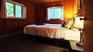 A wooden cabin bedroom with two windows, a bed, and a bedside lamp. - Amenities & Resort Access Included, Cabin 2 (Phelps)