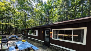 A cabin with a deck, picnic tables, and a stone wall. - Amenities & Resort Access Included, Cabin 2 (Phelps)