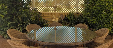 A round table with wicker chairs, a glass top, and a lattice backdrop.