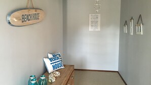 Una habitació amb una banca de fusta, un coixí amb el text 'Beach House' i un cartell que diu 'Beach Rules', a més d'una llista de regles emmarcada a la paret.