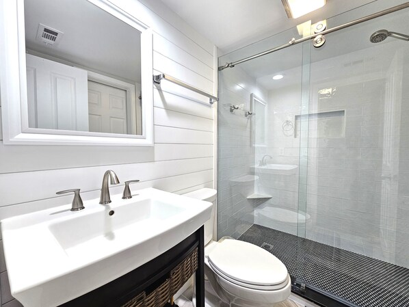 A modern bathroom with a white vanity, a glass shower enclosure, and a toilet.