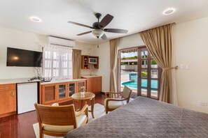A hotel room with a bed, a desk, a chair, a television, a ceiling fan, and a view of a swimming pool.