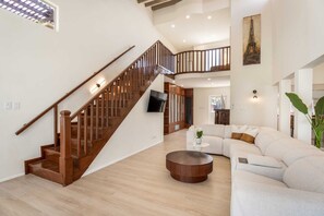 A spacious living area with a wooden staircase, a white sofa, and a round coffee table.