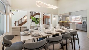 Et moderne spiseområde med et langt bord dækket til seks personer, omgivet af grå polstrede stole.