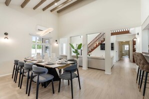 A spacious dining area with a high ceiling, a staircase, and a view of the outdoors.