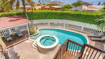 A swimming pool with a hot tub, surrounded by a white fence and lush greenery.