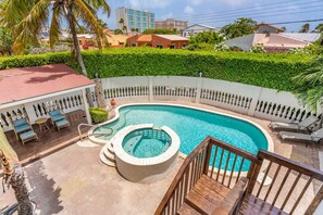 A swimming pool with a hot tub, surrounded by a white fence and lush greenery.