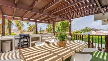 Un patio exterior con una pérgola de madera, una parrilla, una mesa de comedor con sillas y una planta en maceta.