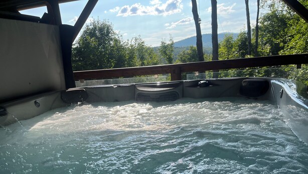 Un jacuzzi con barandilla de madera y vista a árboles y montañas.