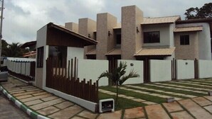 Une maison moderne à deux étages, avec une façade blanche et des touches de couleur beige, dotée d’un petit porche à l’avant et d’une allée pavée.