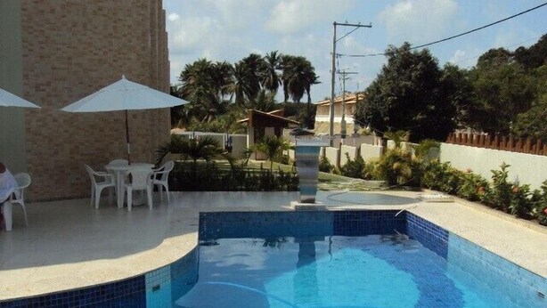 Une piscine dont le bord est revêtu de carrelage, entourée d’un espace de détente extérieur avec des sièges et des parasols.