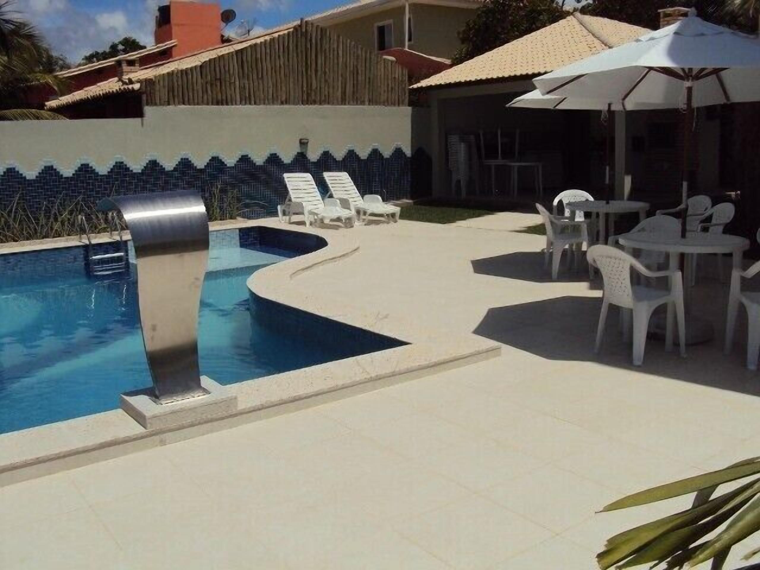 Kaarevareunainen uima-allas, jonka ympärillä on valkoisia aurinkotuoleja ja pöytiä.