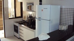Une cuisine de taille réduite avec des meubles blancs, un plan de travail noir, un réfrigérateur blanc, un four à micro-ondes et une cuisinière.