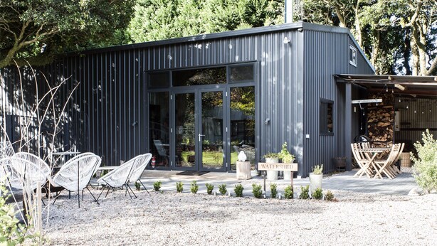 A modern building with a gravel patio, white wicker chairs, and a sign reading "WATERSHEED". - WATERSHED Robertson - a chic shed conversion (Robertson)