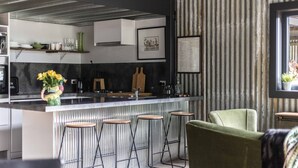 A modern kitchen with a bar area, bar stools, and a green armchair. - WATERSHED Robertson - a chic shed conversion (Robertson)