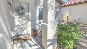 Una casa de fachada color crema, con una puerta principal adornada con un adorno navideño, una ventana y un pequeño jardín con plantas verdes.