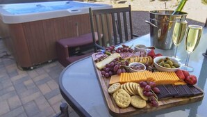 Un jacuzzi, una mesa con una tabla de quesos, galletas, uvas y copas de champán.