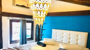 A hotel room with a bed, a white headboard, a hanging lamp, and a window with curtains.