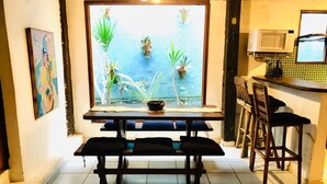 A dining area with a table and benches, a window with a view of greenery, and a kitchen area with a microwave.