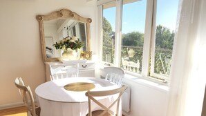 A dining area with a round table, white chairs, a mirror, and a window with a view of greenery. - Little Vella, 2 Bedroom 1 bathroom. Secure parking. Free WIFI. Immaculate clean (Ascot Vale)