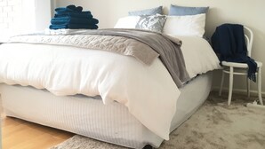 A neatly made bed with a white comforter and a gray blanket, a blue chair with a blanket, and a painting on the wall. - Little Vella, 2 Bedroom 1 bathroom. Secure parking. Free WIFI. Immaculate clean (Ascot Vale)
