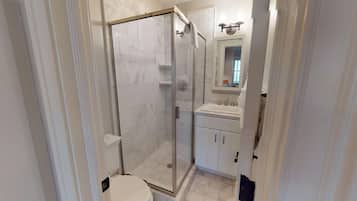 A modern bathroom with a glass-enclosed shower, a sink with a mirror above, and white cabinetry.