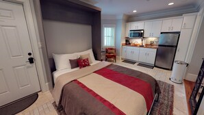 Een slaapkamer met een groot bed, een zithoekje, een kitchenette en een badkamer.
