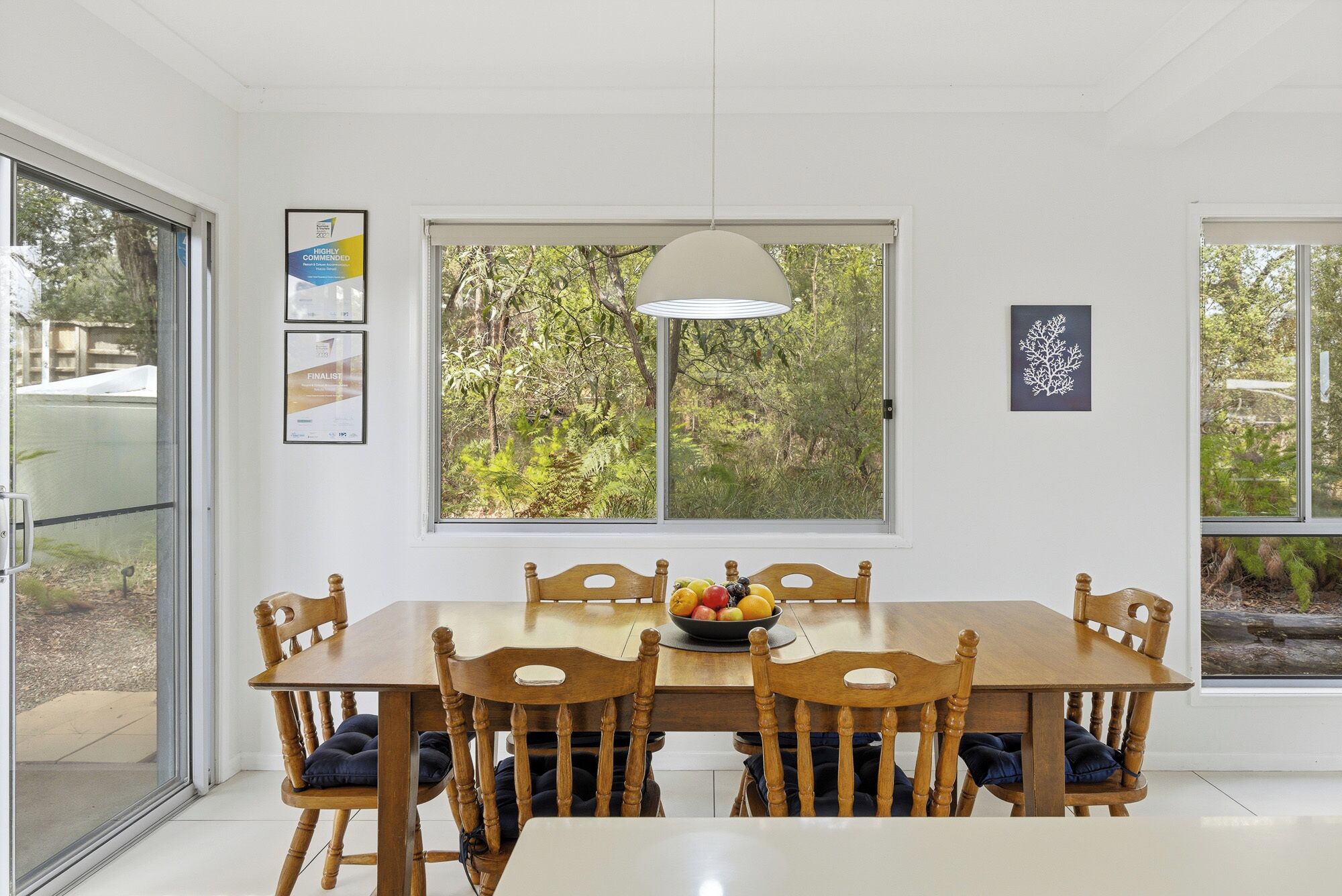 A dining area with a table and chairs, a bowl of fruit, and framed certificates on the wall.