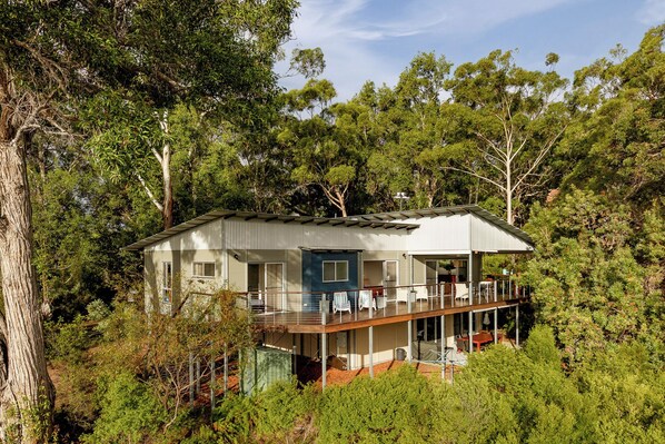 Una casa de dos pisos con un balcón, rodeada de un bosque denso.