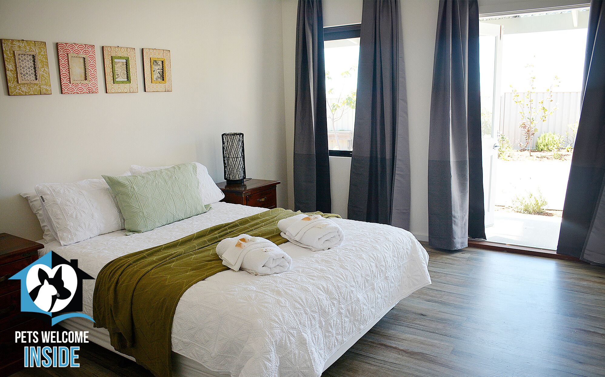 A hotel room with a bed, pillows, a blanket, and towels. There are curtains on the window, and a picture frame on the wall.