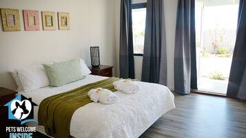 A hotel room with a bed, pillows, a blanket, and towels. There are curtains on the window, and a picture frame on the wall.