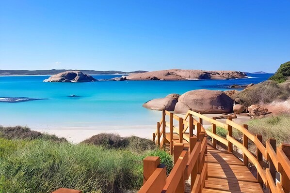 A wooden boardwalk leading to a beach with clear blue waters and large rocks.