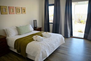 A neatly made bed with a green throw, white pillows, and two towels on the bed.