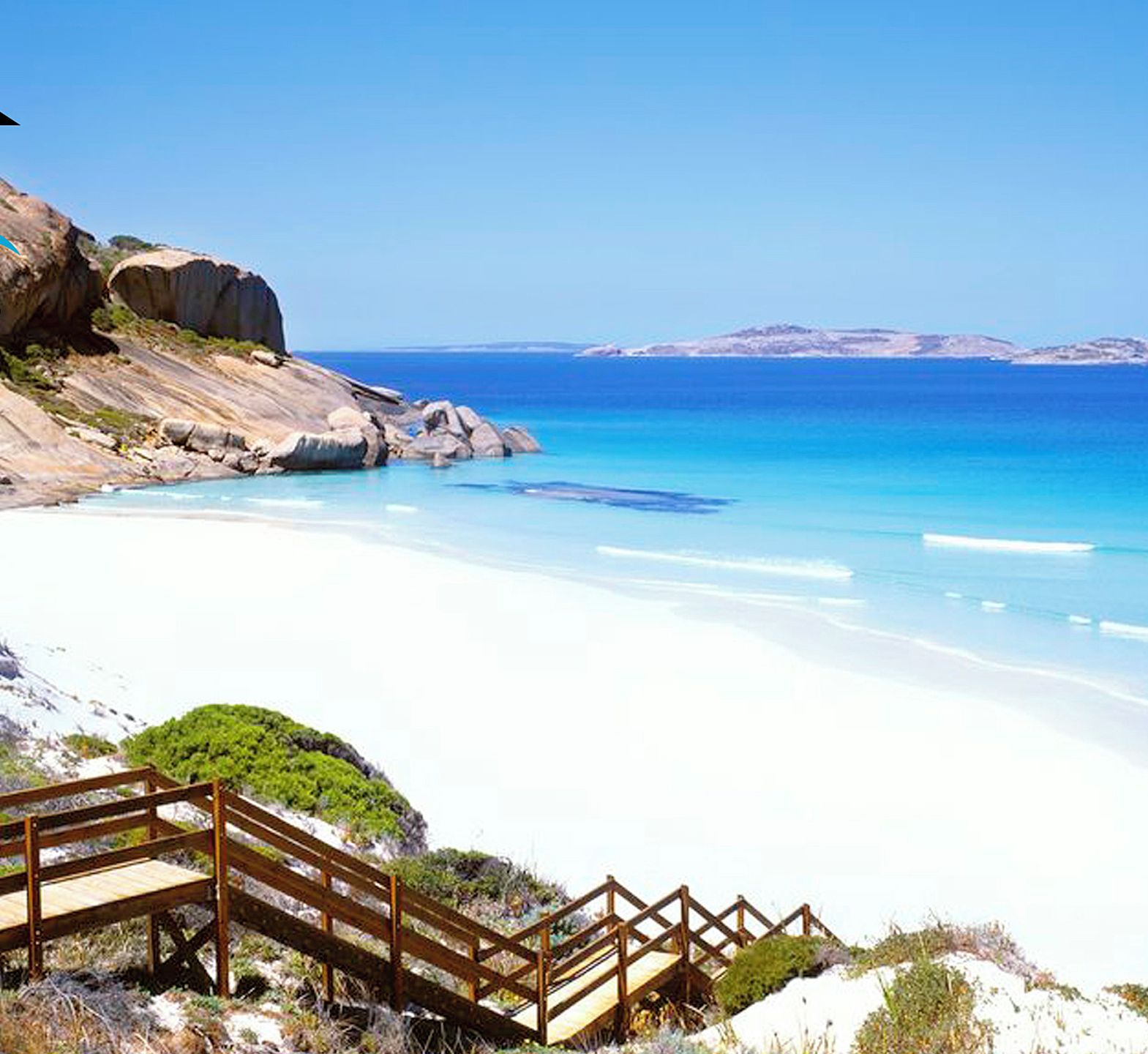 A coastal beach scene with a wooden boardwalk leading to a rocky area.